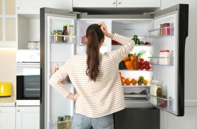 Woman checking the content of her fridge and letting the cold escape