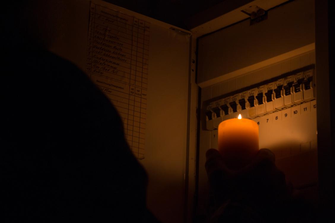 blackout personne éclairant son compteur électrique à la bougie