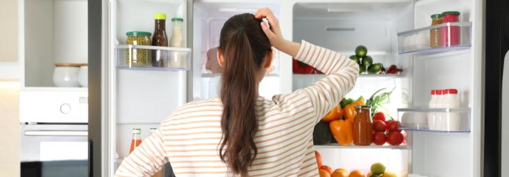 Woman checking the content of her fridge and letting the cold escape