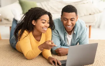 Couple regardant les prix de l'énergie sur un ordinateur portable avec le sourire