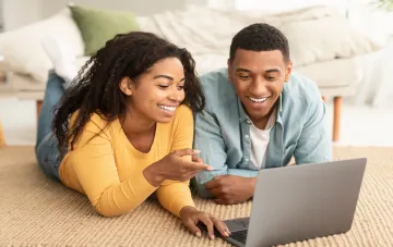 Couple regardant les prix de l'énergie sur un ordinateur portable avec le sourire