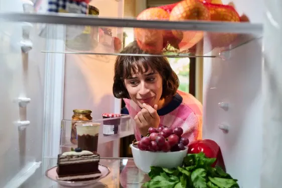 Femme regardant ce qui se trouve dans son frigo et hésitant sur son choix