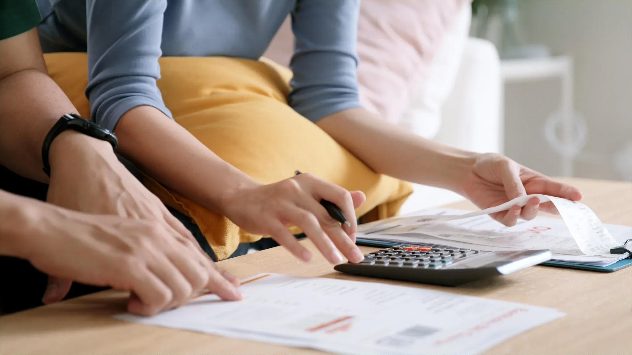 Mains d'un couple tenant une calculatrice et comparant des papiers sur une table devant eux