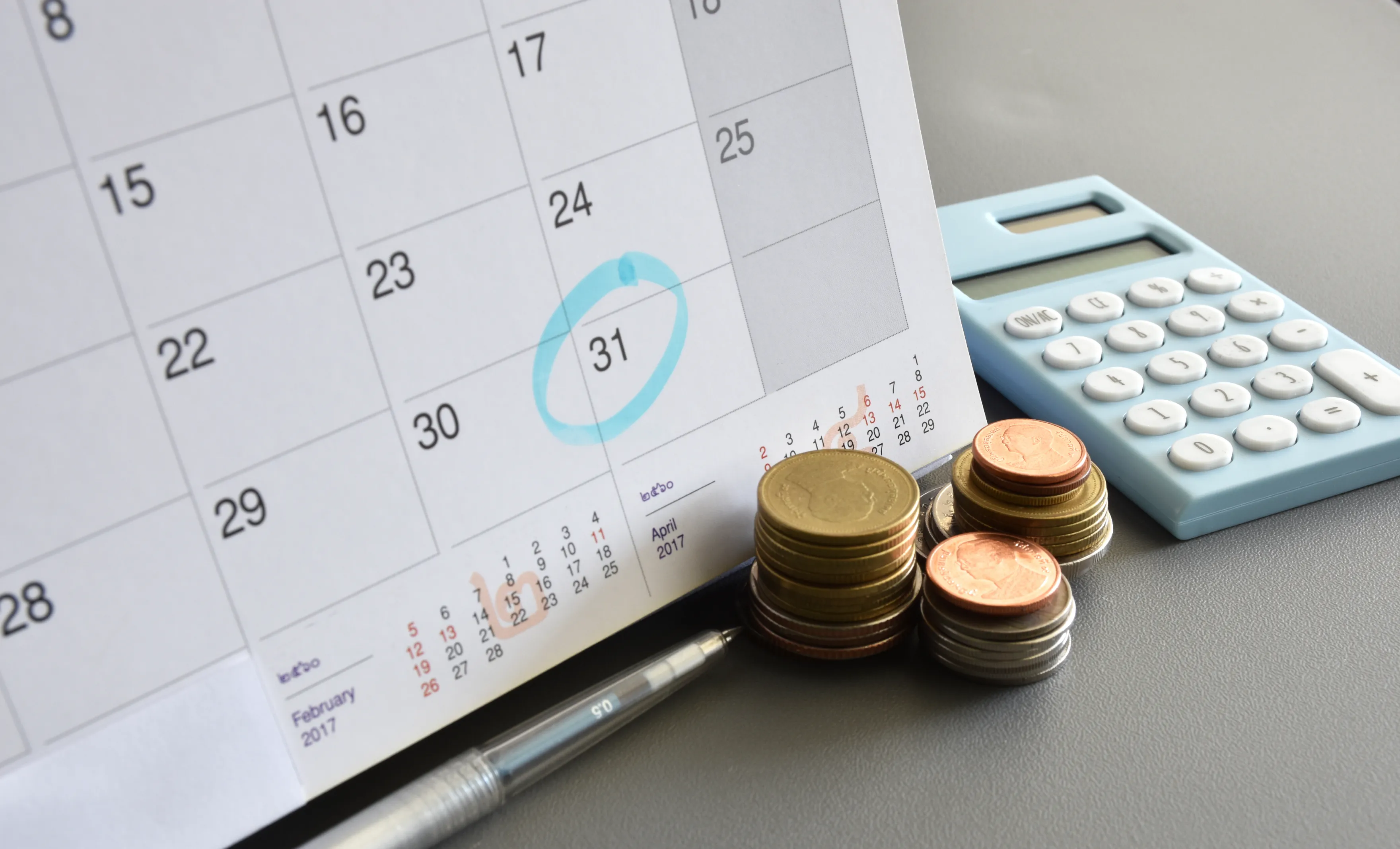 Calendrier avec le dernier jour du mois entouré, près d'une calculatrice et d'une pile de monnaie